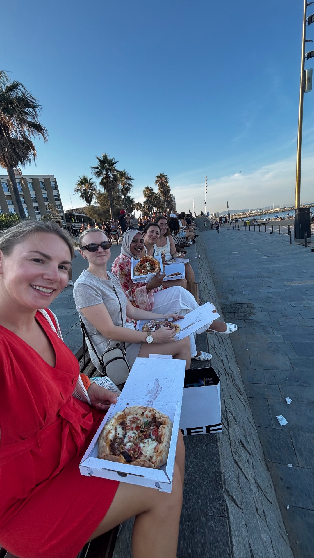 Friends eating pizza on the Barceloneta seafront at golden hour